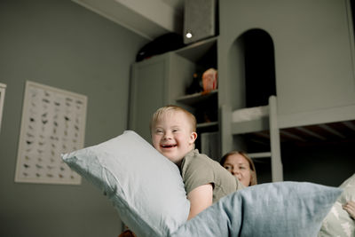 Side view of happy boy playing with pillows in bedroom at home