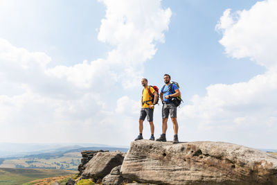 Low angle view of men standing on rock against sky