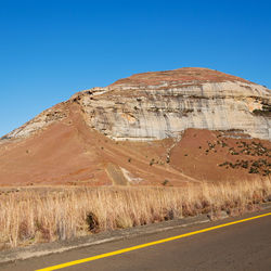 Scenic view of road by mountains against clear blue sky