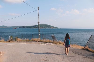 Rear view of man standing at sea shore against sky