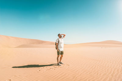 Full length of young woman standing in desert against clear sky