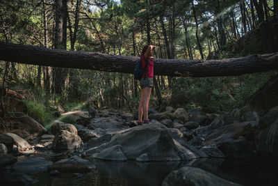 Full length of woman standing on rock by stream in forest