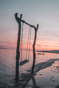 Silhouette wooden posts on beach against sky during sunset