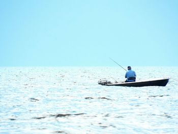 Man in fishing boat against clear sky