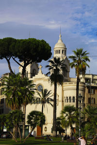 Low angle view of trees by buildings in city against sky