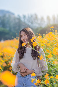 Smiling woman standing by yellow flowering plants