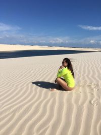Side view of young woman sitting on sand dunes at desert