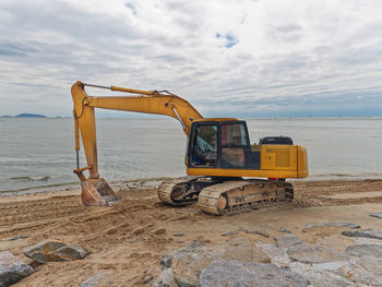 Yellow excavator working on the beach against sea water and cloudy sky
