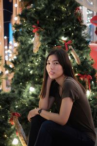 Portrait of young woman by illuminated christmas tree