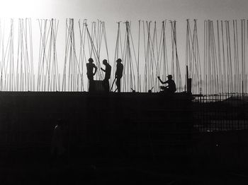 Silhouette people against sky seen through fence