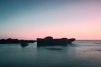 Silhouette rocks in sea against clear sky during sunset