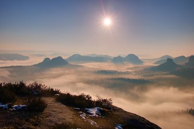 Scenic view of misty mountains and valley against sky during sunset