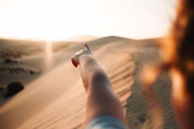 Close-up of woman pointing in desert during sunset