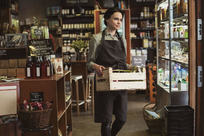 Smiling owner carrying vegetable crate while walking in store