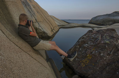 Man on rock at beach against sky