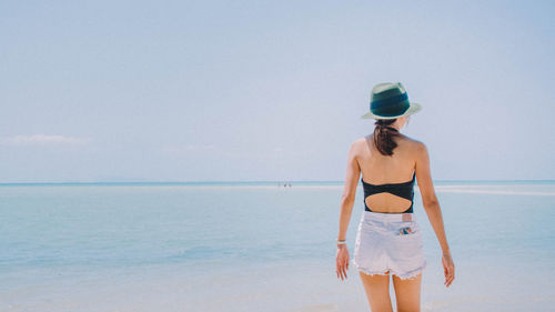 Rear view of woman standing at beach against sky