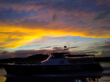 Boats moored in sea against dramatic sky during sunset