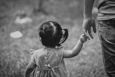 Midsection of man holding hands with daughter while walking on field