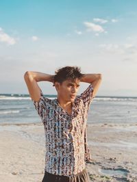 Man looking away while standing at beach against sky