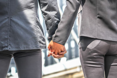 Midsection of colleagues holding hands in city