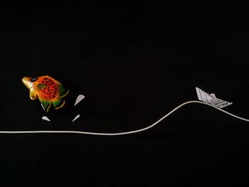 Artificial fish with paper boat and cable against black background