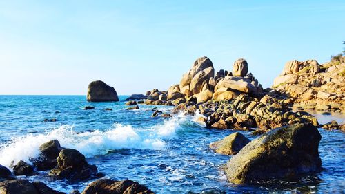 Rocks in sea against clear blue sky