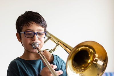 Boy playing trombone against wall