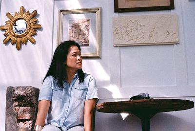 Mature woman looking away while sitting against wall