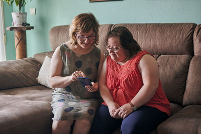 Adult woman and her sister with down syndrome look at a phone at home