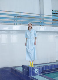 Smiling teenage girl looking away while standing at poolside against wall