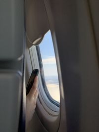 Cropped hand of woman using smart phone by window in airplane