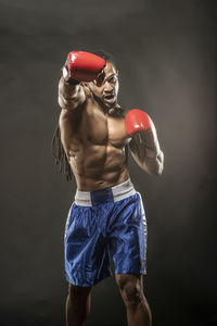 Portrait of shirtless boxer punching against black background