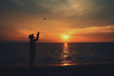 Silhouette man standing on beach against orange sky