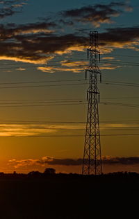 Low angle view of silhouette electricity pylon on field against sky during sunset