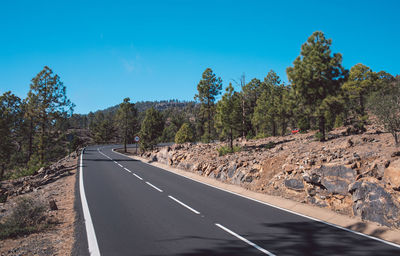 Road by trees against blue sky