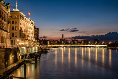 Illuminated buildings by river against sky at night