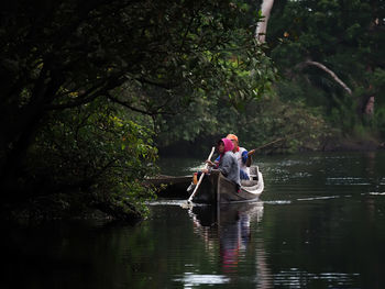 People in boat on river amidst trees in forest