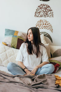 Young caucasian charming pregnant brunette sitting on the bed in home clothes in the lotus position.