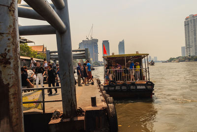 People at commercial dock against sky in city