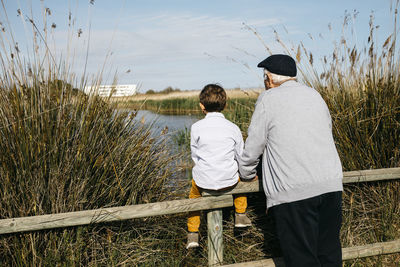 Back view of little boy and his grandfather looking at a lake