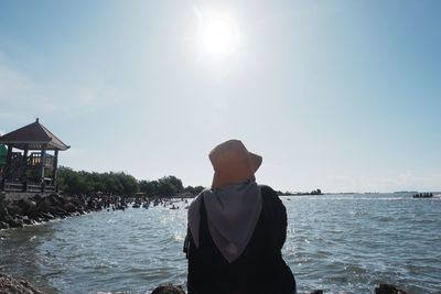 Rear view of women sitting by sea against sky