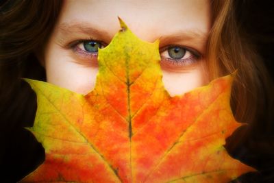 Close-up portrait of woman covering face with autumn leaf