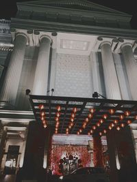 Low angle view of illuminated lighting equipment hanging on building