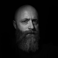 Close-up portrait of bearded mature man against black background