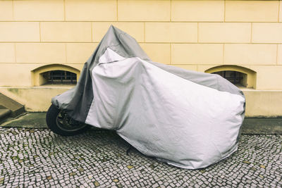 Motorcycle covered with fabric parked against wall