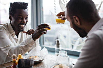 Happy friends toasting drinks while sitting at table in restaurant