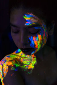 Close-up of young woman with paint on face and body in darkroom