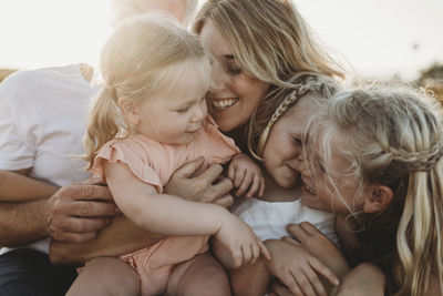 Lifestyle close up of family with young sisters sitting on beach