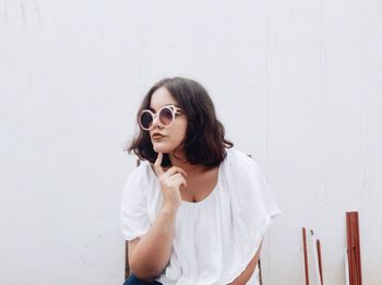 Woman wearing sunglasses posing against white wall