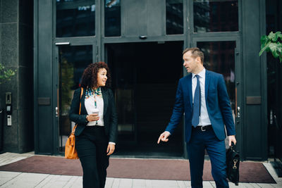 Businessman and businesswoman walking while talking against building in city